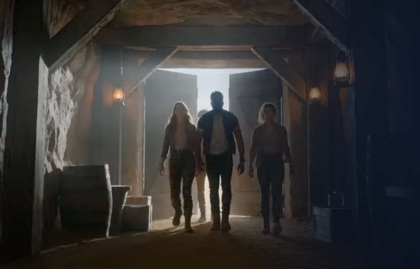 Three people walking into a dimly lit, rustic wooden structure.